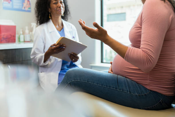 Unrecognizable pregnant woman gestures while talking to obstetrician The unrecognizable mid adult expectant mother gestures as she talks to the smiling mature adult female doctor. midwife photos stock pictures, royalty-free photos & images