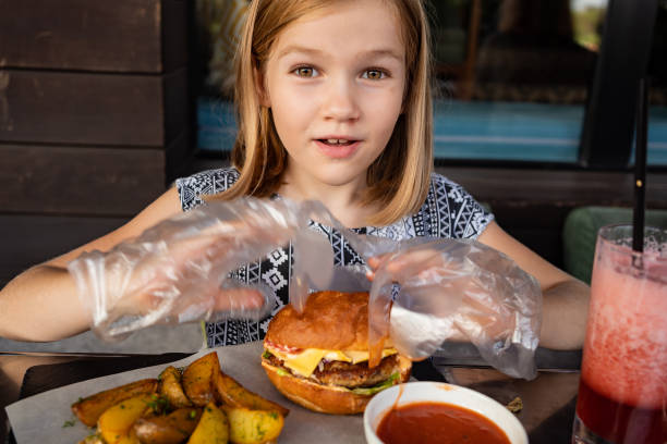 a little girl with gloves eats a burger and potatoes in a summer outdoor cafe.