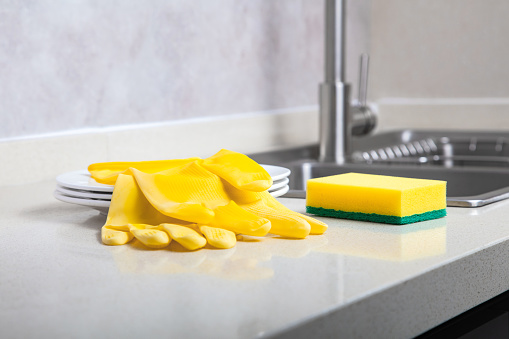 Yellow cleaning sponge and rubber gloves by the kitchen sink，Housework concept
