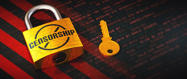 Extreme close-up on a yellow padlock and key, with a label 'censorship', lying on striped digital surface with glowing words. Close up, wide horizontal composition.