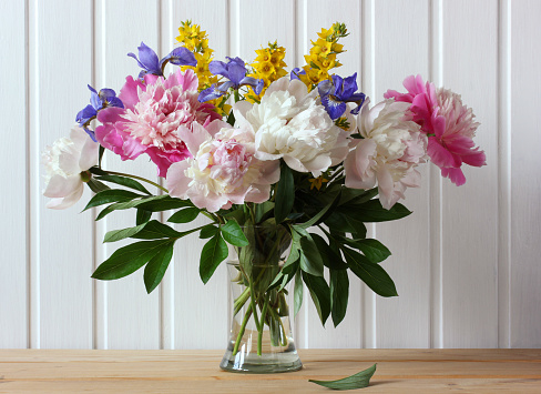 spring garden flowers in a glass vase peonies and irises on a wooden table