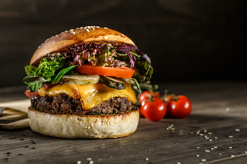 Closeup photo of home made fresh burger with beef, onion, tomato, lettuce, cheese and spices.burger on the board on a dark background