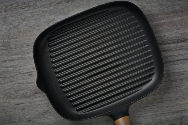 istock Square empty frying pan on wooden table background. Griddle utensils for grilling meat or vegetable. Top view with copy space for text. 1340104631