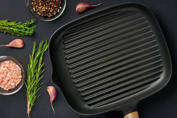 istock Square empty frying pan on black table background with spices and seasoning. Griddle utensils for grilling meat or vegetable. Top view with copy space for text. 1340104827