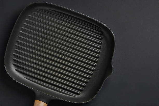 Square empty frying pan on black table background. Griddle utensils for grilling meat or vegetable. Top view with copy space for text.