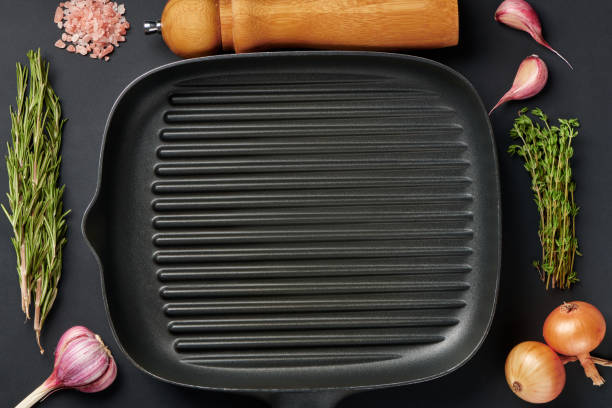 istock Square empty frying pan on black table background with spices and seasoning. Griddle utensils for grilling meat or vegetable. Top view with copy space for text. 1340104989
