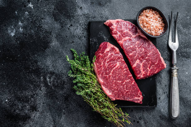 istock Fresh Raw Denver steak Marble beef meat with herbs. Black background. Top view. Copy space 1340109277