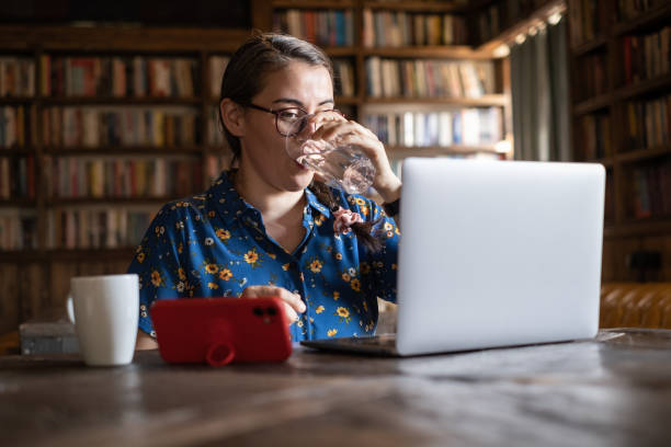 Woman drinking water and working on laptop at library stock photo