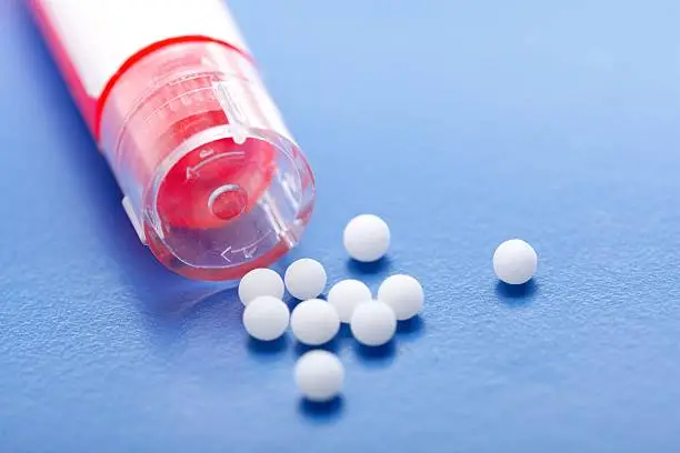 Modern homeopathic pills and plastic container on blue background