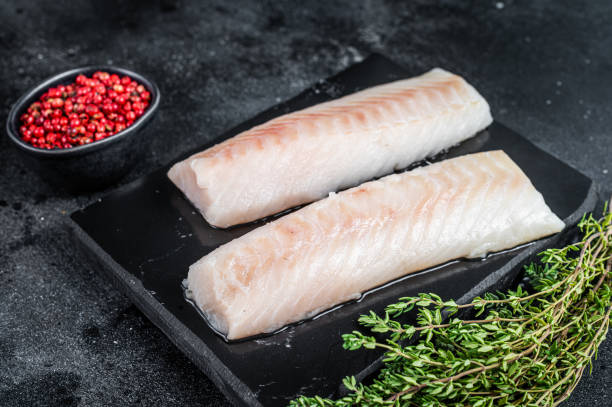 istock Raw cod loin fillet fish on marble board. Black background. Top view 1340111394