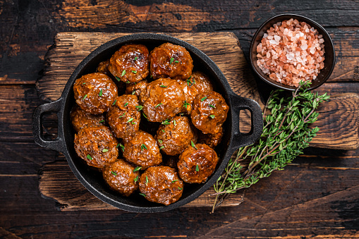 Meatballs in tomato sauce from beef and pork meat with thyme in rustic pan. Dark background. Top view.