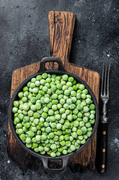 istock Fresh Frozen green peas in a pan. Black background. Top view 1340113309