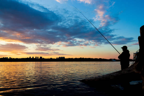 Krasnoyarsk, Russia - July 01, 2021: fisherman fishing in the river at sunset against the background of the city silhouette