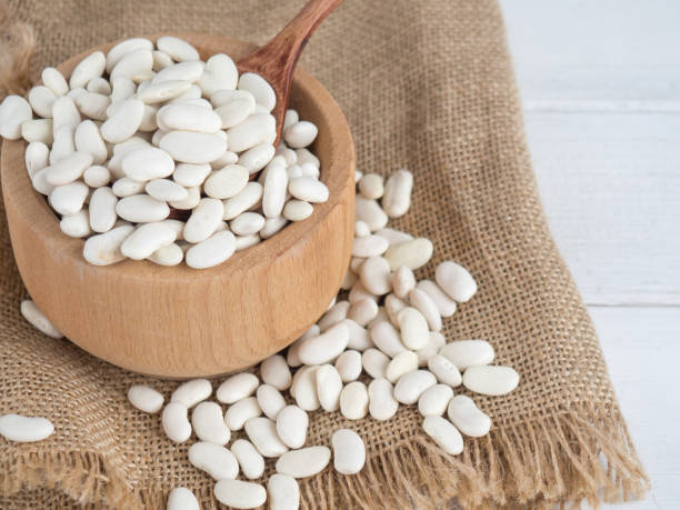 istock white beans in a wooden spoon on a white wooden table, copy space 1340119885