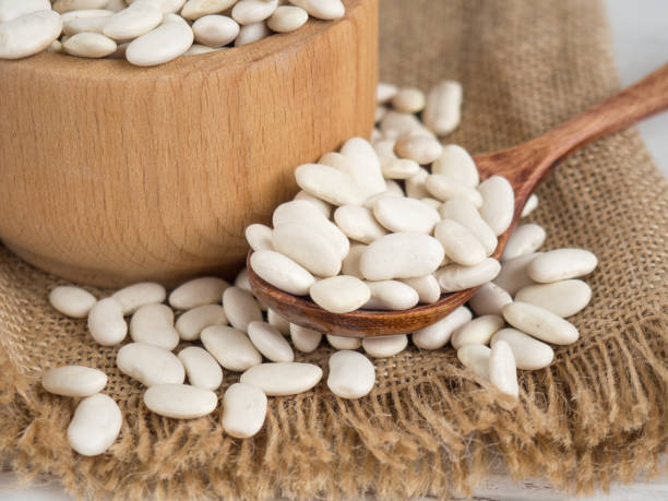 istock white beans in a wooden spoon on a white wooden table, copy space 1340119886