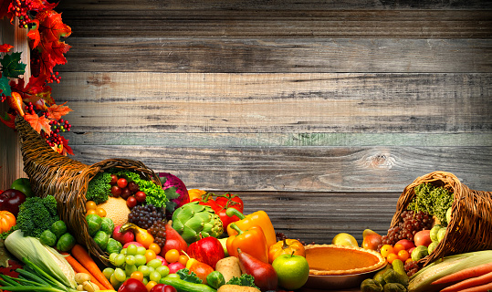 A Thanksgiving cornucopia of fruits and vegetables rests on a table in front of a background of wooden planks.
