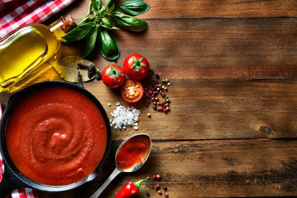 Photo of Table top view of ingredients to prepare pasta and tomato sauce in a domestic rustic kitchen with copy space