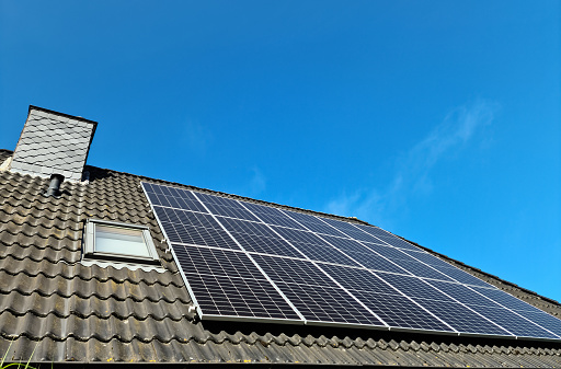 Solar panels producing clean energy on a roof of a residential house with black roof tiles.