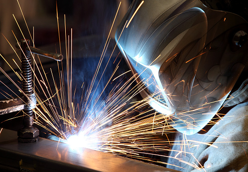 A welder welding two pieces of metal together in a metal fabrication facility.
