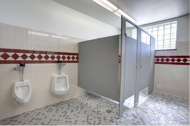 The interior of a public men's restroom The interior of a clean, modern, public, men's restroom with toilet stalls, and urinals, flushing valve public restroom toilet stock pictures, royalty-free photos & images