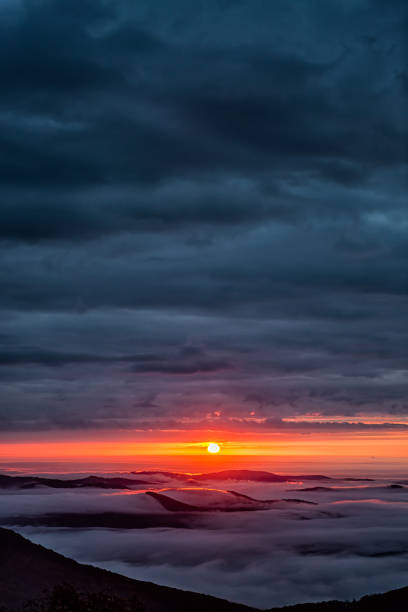 dunkle wolken bei sonnenaufgang morgens vertikale ansicht im wintergreen resort, virginia skiort mit bunter roter sonne am horizont mit sonnenlicht himmel in blue ridge mountains - vertical horizon over land beauty in nature beautiful stock-fotos und bilder