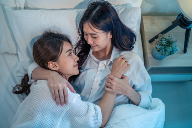 istock Asian beautiful lesbian couple lying down on bed and hugging each other. Attractive romantic girl friend in pajamas spending night leisure time together in bedroom in house. Homosexual-LGBTQ concept 1340143990