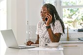 Multitasking black woman talking on the phone and working on the computer at home