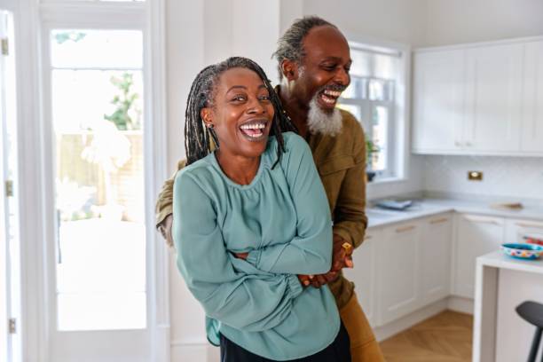 Vibrant senior couple embrace and laugh while relaxing at home A healthy and happy black senior couple laugh while embracing. The retired active seniors are enjoying a relaxing day at home together. Aging process, retirement, family lifestyle and active seniors concepts middle aged couple dancing stock pictures, royalty-free photos & images