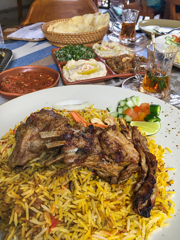 Close-up shot of Indian lamb biryani ( yellow rice ). In the background there's some variation condiments such as hummus, baba ghanoug,thabullah. As for drinks , there's a Moroccan mint tea.