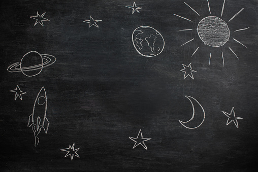 Planets and stars drawn on the blackboard. There is also a rocket flying in space.
