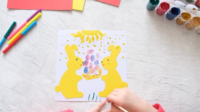 Child making card with Easter bunnies  from colorful paper. Applique. Handmade. Project of children's creativity, handicrafts, crafts for kids.