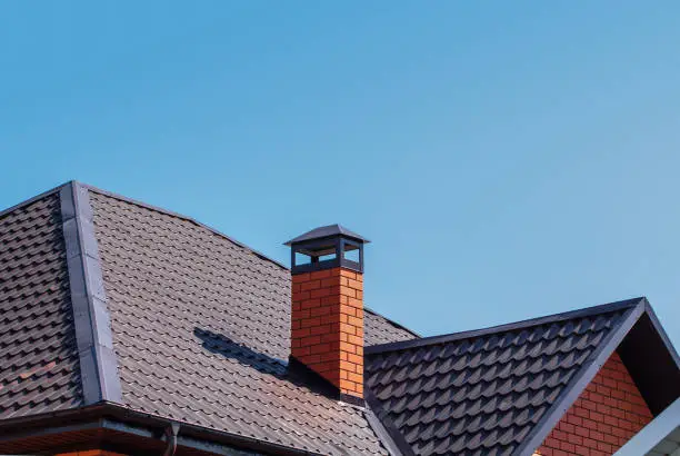 Photo of Brick chimney pipe on metal roof of a private house against the sky