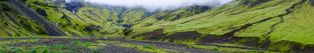 Panorama landscape view from  south coast of Iceland. Top green grass and moss above black lava with a lot of streams, rapids and small waterfalls on foggy and cloudy weather.