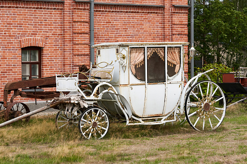 Old white carriage on the background of a red brick building. White vintage carriage