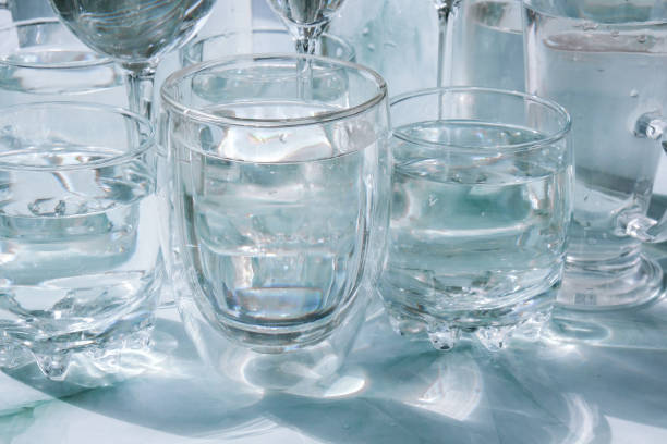 istock Beautiful different glasses stand on white background in sunlight and create shadows. Hard light, long shadows. Creative concept of drinks, alcohol cocktails. Glassware concept 1340170567