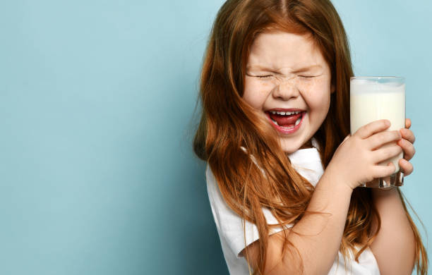 Cute red hair girl child kid drinking milk or kefir screaming joyfully with closed eyes on light blue background. Health and diet stock photo