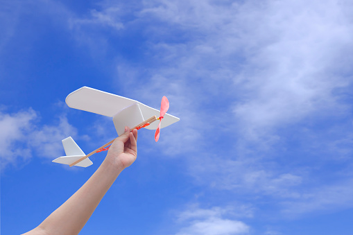 Child hand playing rubber powered aircraft against cloud on blue sky background