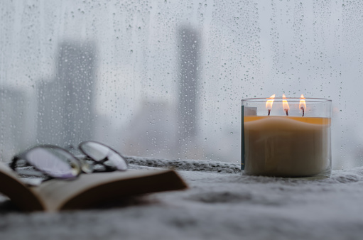 Burning aroma candle puts near by window that have rain drop in monsoon season with blurred city background. Zen and relax concept.