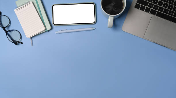 istock Above view smart phone, laptop computer, notebook and coffee cup on blue background. 1340181310