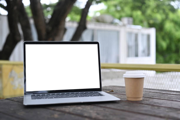 istock Mock up computer laptop and coffee cup on wooden table at outdoor. 1340181861