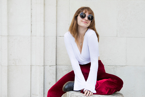 Portrait of an attractive female student wearing red flare pants, a white top and sunglasses - outdoors in summer