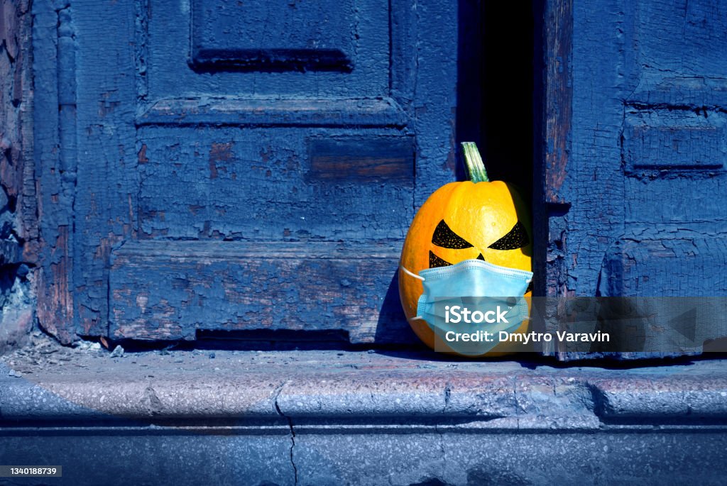 Halloween background. A naughty pumpkin wearing in a medical mask peeking out from behind an old abandoned door. Door Stock Photo