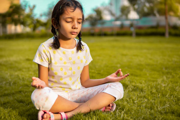 индийская маленькая девочка, занимающаяся йогой в парке. - zen like nature breathing exercise sitting стоковые фото и изображения