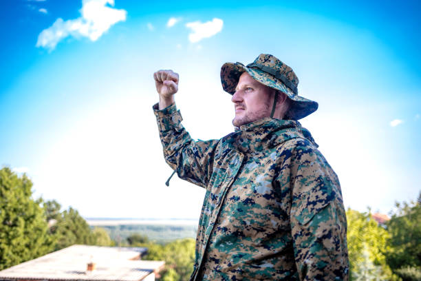Rear view image of a Military man standing on top of terrace and scouting. Cropped shot of a male army soldier saluting against blue sky. Soldier in the mountain forest, celebrating freedom.