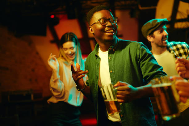 Cheerful African American man dancing during his night out in a pub. Young happy black man having fun while dancing with his friends in a bar at night. black people bar stock pictures, royalty-free photos & images