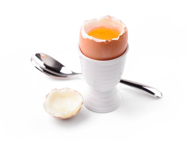 Soft boiled egg with egg cup and spoon isolated on white background, close-up.