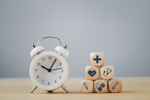 white analog alarm clock and health and medical icon on wooden cube, awareness , wellness, wellbeing, time for health checking, annual checking concept