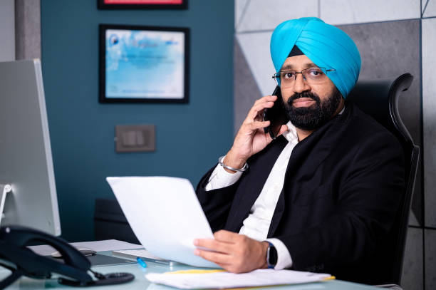 istock Mid Adult Sikh businessman working on computer and checking important papers/Bill and Making phone Call Sitting At Desk In Office 1340199766