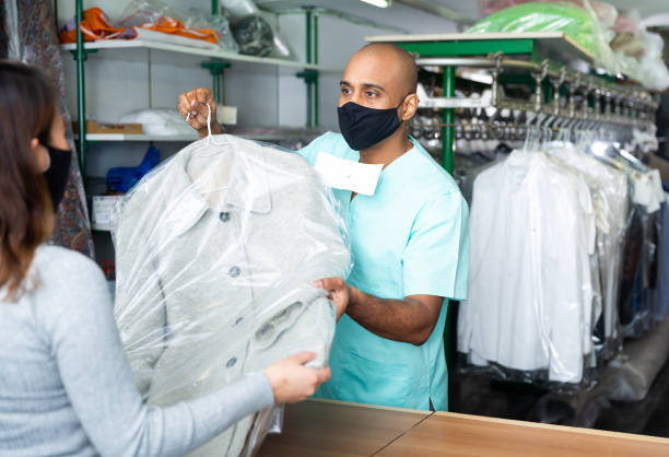 istock Male employee in protective mask with client in modern laundry, returning clothing after cleaning 1340205402