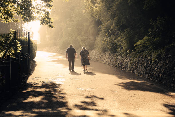 Senior couple watching sunset on trail in park; man hugging woman